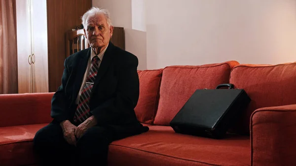 Älterer Großvater - trauriger alter Großvater sitzt auf einem Sofa und blickt in die Kamera — Stockfoto