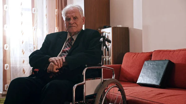 Elderly grandfather - sad grandfather is sitting in a wheelchair in his room and looking at the camera — Stockfoto