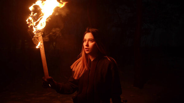 Young amazed woman traveler walking in the woods at night holding a torch
