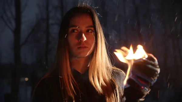 Jovem morena com tocha em pé na floresta de inverno sob a queda de neve — Fotografia de Stock