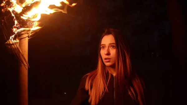 Giovane donna che tiene la torcia di fuoco in piedi nella foresta oscura — Foto Stock
