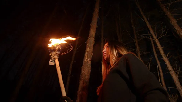 Молодая потерянная женщина с длинными волосами стоит в зимнем лесу ночью с факелом ручной работы — стоковое фото