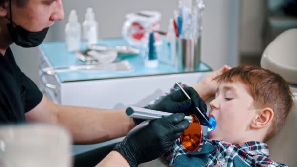 Een kleine jongen die zijn tanden laat doen - de fotopolymeerlamp in de mond steken en het licht aandoen — Stockvideo