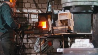 Blacksmith working - putting a longer piece of metal under the pressure of industrial forging machine