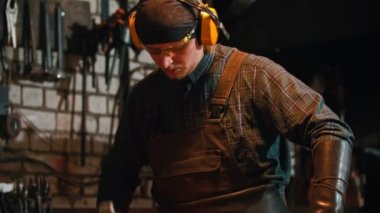 Demirci atölyede çalışıyor. İşçi çekiçle metal parçasına vuruyor.