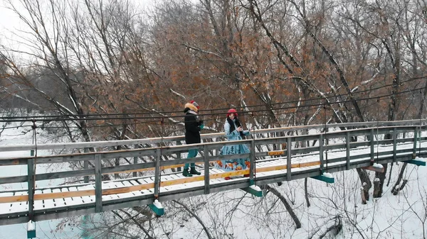 Дві молоді жінки друзі п'ють гарячі напої з термоса і ходять по засніженому мосту — стокове фото