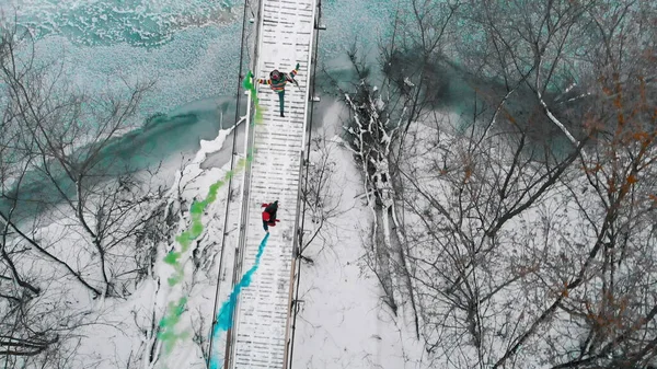 Two women running on the snowy bridge holding green and blue smoke bombs — Stockfoto