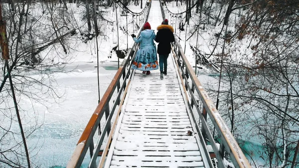 Two young women in down jackets drinking hot drinks and walk on the bridge — 스톡 사진