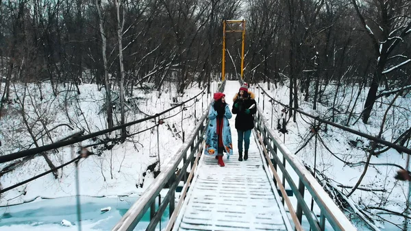 Two young women students drinking hot drinks and walk on the snowy bridge — 스톡 사진