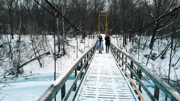 Two young women students drinking hot drinks and walk on the snowy bridge in the forest — Stockfoto