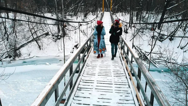 Two young women students drinking hot drinks and walk on the snowy bridge in the winter forest — 스톡 사진