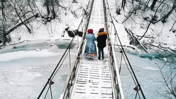 Two young women students drinking hot drinks and walk on the bridge in the winter forest — Stockfoto