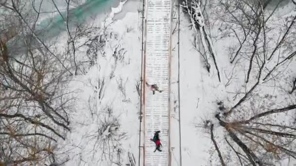 Two colorful young women running on the snowy bridge and having fun with each other — Stockvideo