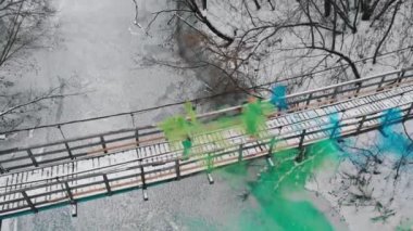Karlı köprüde iki kadın yeşil ve mavi sis bombalarıyla eğleniyor.