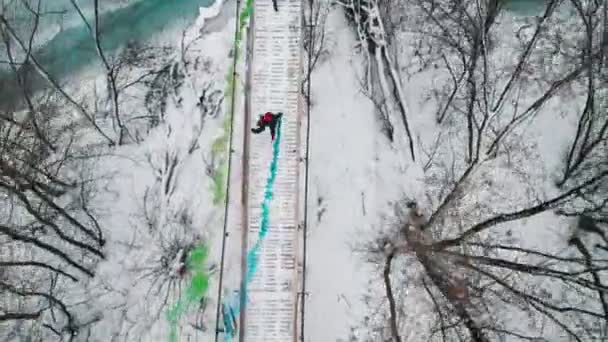 Two women running on the snowy bridge holding colorful smoke bombs — 图库视频影像