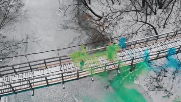 Twee vrouwen op de besneeuwde brug hebben plezier met groene en blauwe rookbommen — Stockvideo