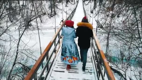 魔法瓶から熱い飲み物を飲んで雪の橋を歩く2人の若い女性 — ストック動画