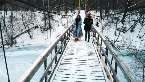 Two young women drinking hot drinks and walk on the winter bridge — Αρχείο Βίντεο