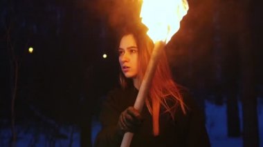 A beautiful woman waving with torch standing in winter forest