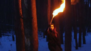 Young scared woman with torch walk in the dark forest