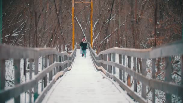 Two young women running on the snowy bridge — Wideo stockowe