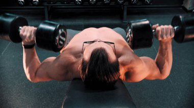 Vücut geliştiren bir adam spor salonundaki kürsüde ellerini sallıyor.