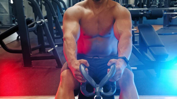 Ein attraktiver Mann Bodybuilder macht Kraftübungen in der Sporthalle - ziehen Sie das Gewicht in Neonlicht — Stockfoto
