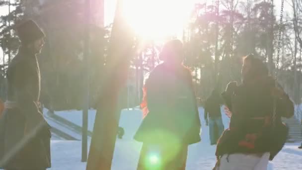 La gente rusa - mujer en traje popular está montando en un columpio en un parque de invierno en tiempo soleado — Vídeo de stock