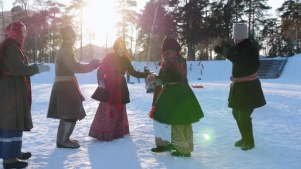 Folclore russo - homens e mulheres em trajes populares russos estão dançando em pares em um parque de inverno — Vídeo de Stock