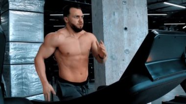 Çekici bir vücut geliştirici koşu bandında koşuyor ve değişim modlarını değiştiriyor.