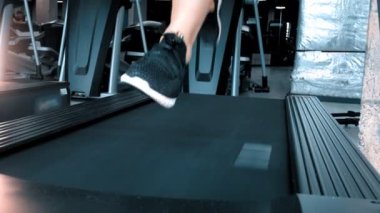 Spor salonundaki koşu bandında koşan spor ayakkabılı bir adam.