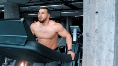 Sakallı çekici genç bir vücut geliştirme ustası koşu bandında çabalayarak koşuyor.