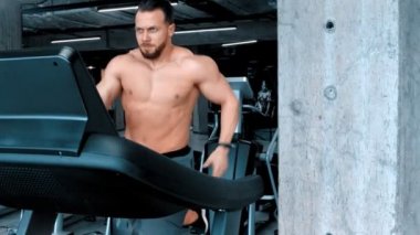 Sakallı, çekici, genç bir vücut geliştirici. Koşu bandında koşuyor. Modern spor salonunda çabalıyor.