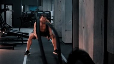 Genç bir vücut geliştirme ustası gayretle iplerle boğuşuyor.