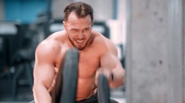 Genç ve çekici bir vücut geliştirme ustası spor salonunda halatlarla boğuşuyor.