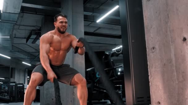 Ein junger attraktiver Mann Bodybuilder kämpft mit Anstrengung gegen Seile — Stockvideo