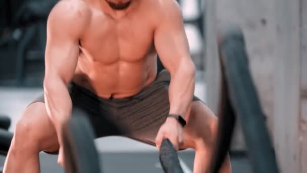 Un joven hombre atractivo culturista luchando cuerdas con un esfuerzo en el gimnasio — Vídeos de Stock