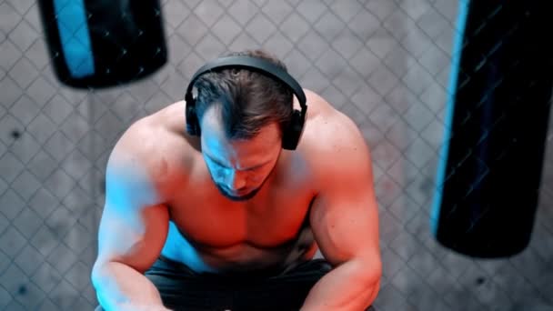 Atraktivní muž boxer ve sluchátkách sedí na lavičce a pitné vody — Stock video