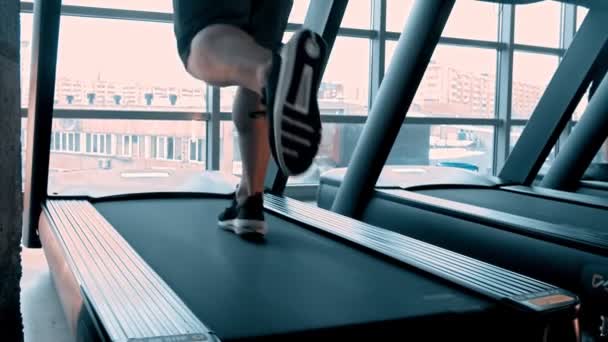 Человек в кроссовках бегает по беговой дорожке в современном тренажерном зале с панорамными окнами — стоковое видео