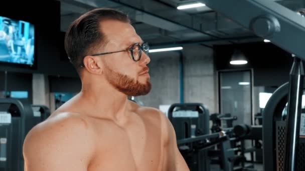 En skäggig man kroppsbyggare i glasögon gör styrketräning i gymmet — Stockvideo