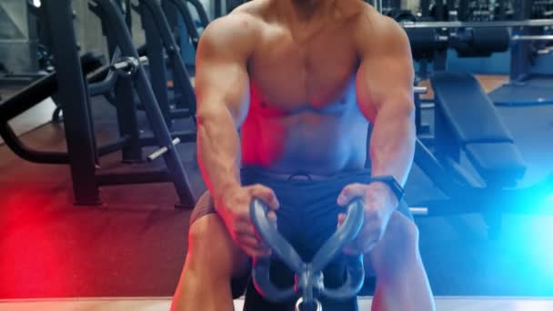 Een bebaarde aantrekkelijke man bodybuilder doet krachtoefeningen in de sportschool - trekken het gewicht in neon verlichting — Stockvideo