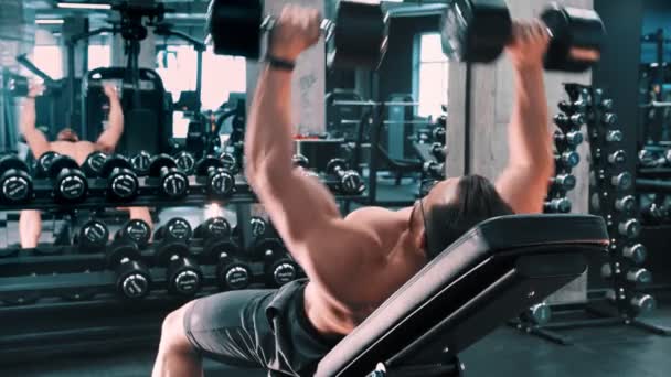 Een man bodybuilder pompen zijn handen spieren liggend op de tribune — Stockvideo