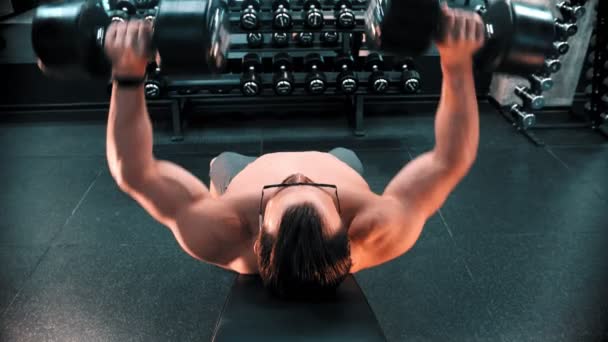 Ein Mann Bodybuilder mit Brille pumpt seine Hände Muskeln liegend auf dem Stativ in der Turnhalle — Stockvideo