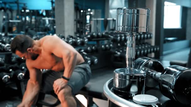 Een man bodybuilder pompen zijn hand spieren zitten in de sportschool — Stockvideo