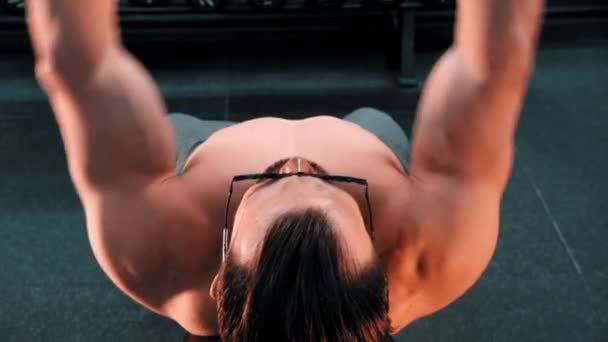 A fit man bodybuilder in glasses pumping his hands muscles with dumbbells lying on the stand in the gym — Stock Video