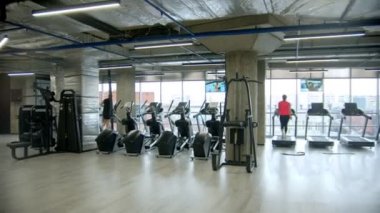 Spor salonunda büyük camlı pencerelerle egzersiz yapan insanlar.