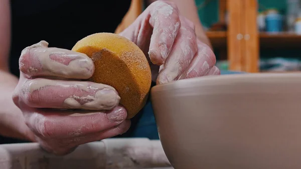 Кераміка - майстер протирає гончарне колесо жовтою губкою — стокове фото