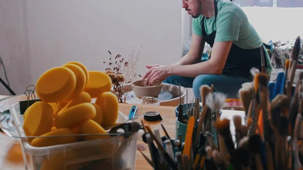 Pottery - mistr v zeleném tričku sedí ve své dílně mezi svými nástroji — Stock fotografie