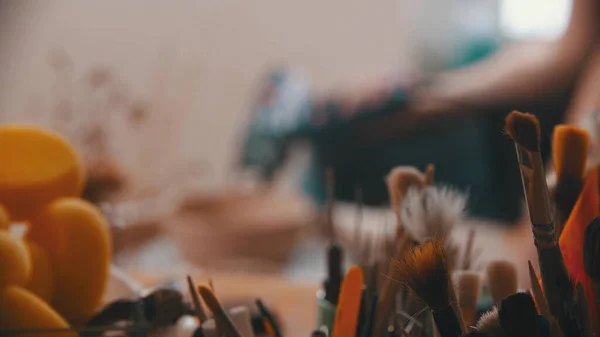 Керамика - мастер сидит в мастерской среди своих инструментов и вымирает из чаши. дефокусировка — стоковое фото
