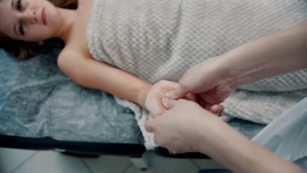 Massaggio massaggiatrice sta impastando le dita sul palmo di una giovane donna su un divano — Video Stock